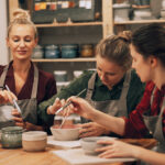 A company of three cheerful young women friends are painting ceramics in a pottery workshop. Lifestyle concept.